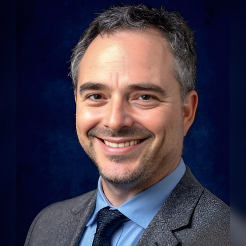 A man in a suit and tie smiling for the camera.